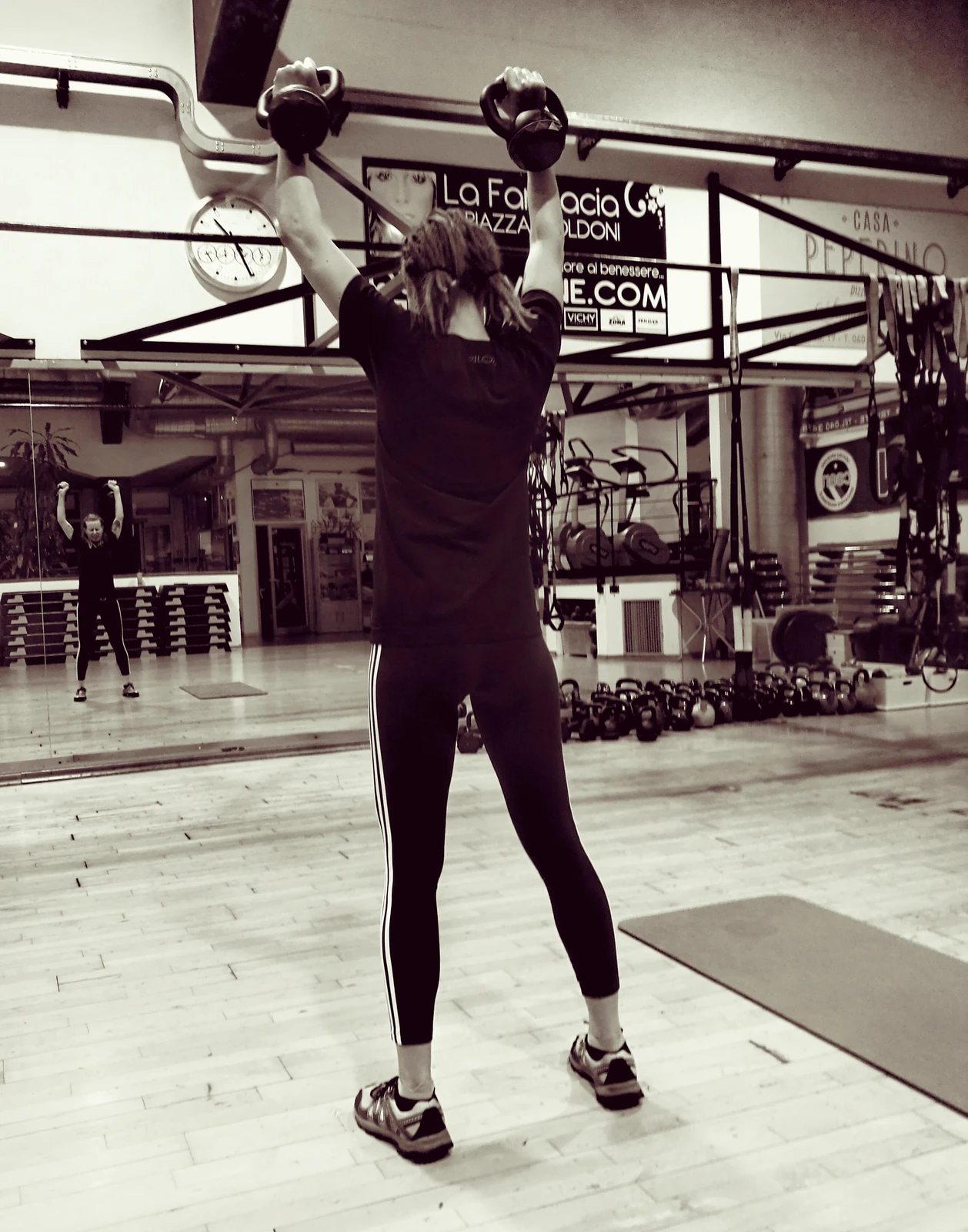 Una cliente solleva due kettlebell sopra la testa in palestra